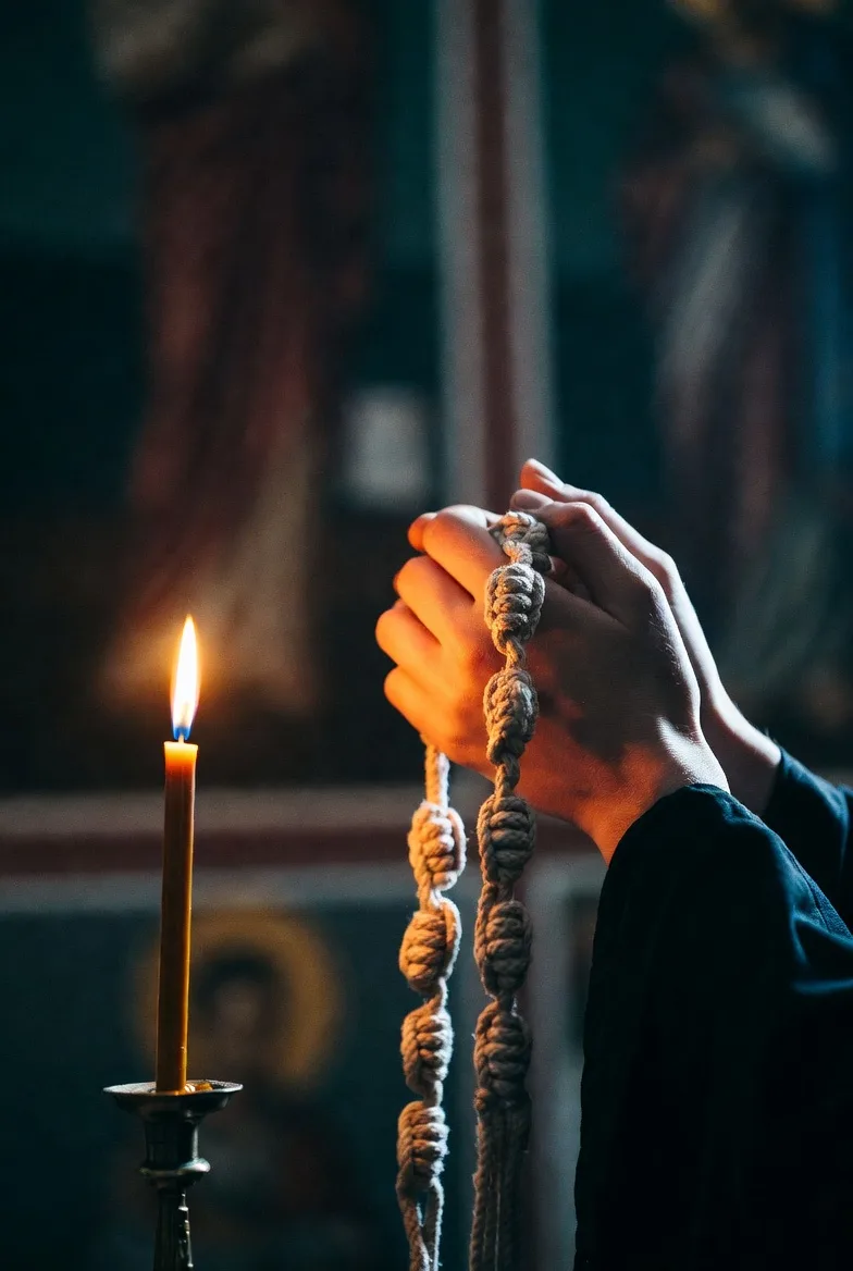 Hands holding a prayer rope beside a lit candle