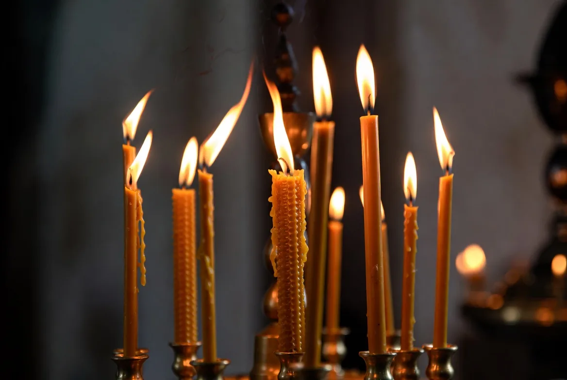 Tall thin candles burning in a dark church
