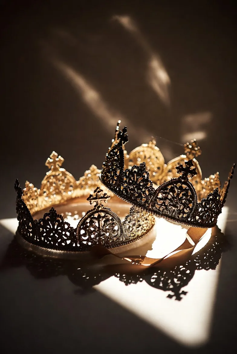 Two ornate metal wedding crowns lying in a beam of light