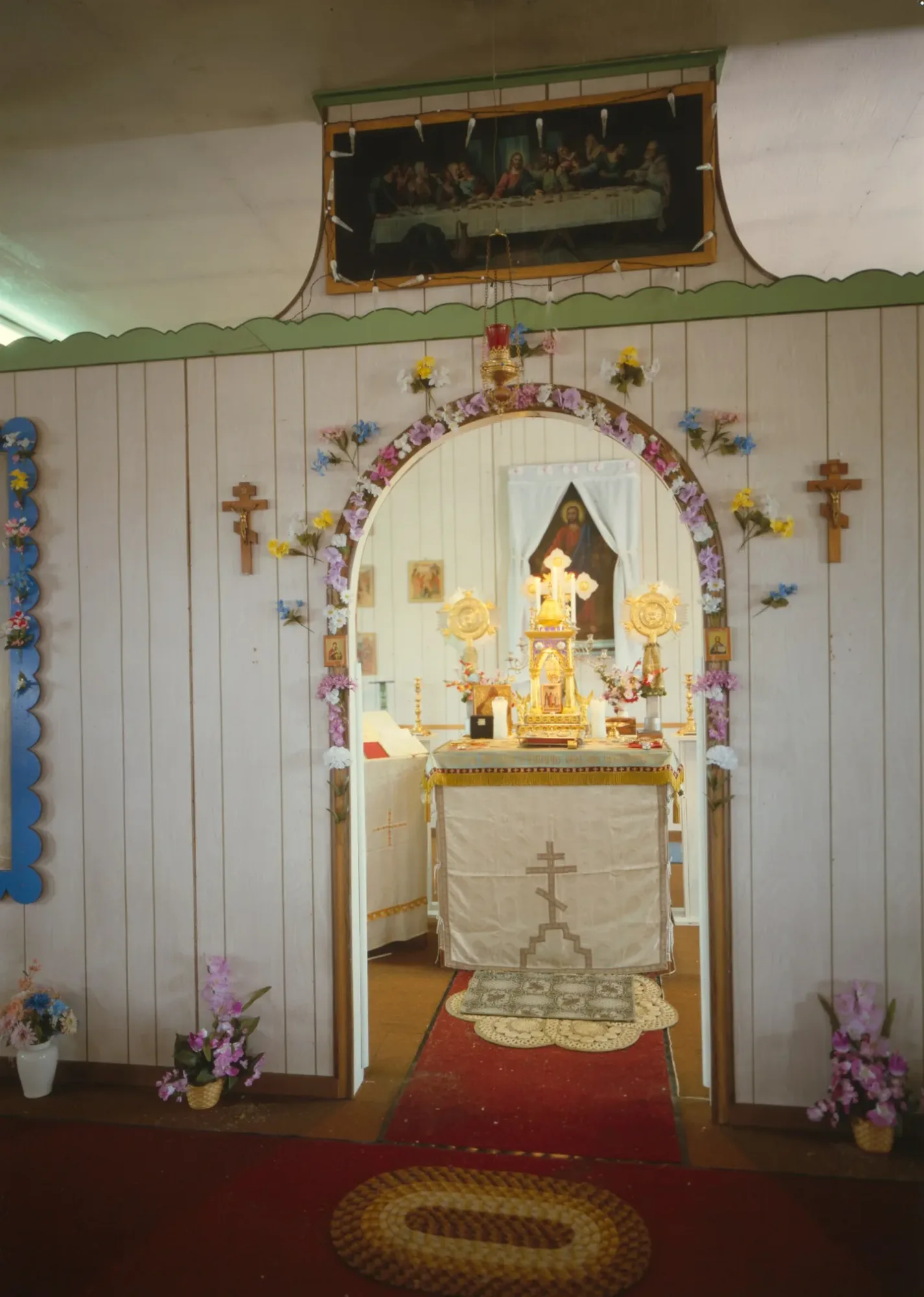 Through an arched doorway in the iconostasis: the altar, with the holy table covered in a cloth marked with a cross, candles and the tabernacle on it.