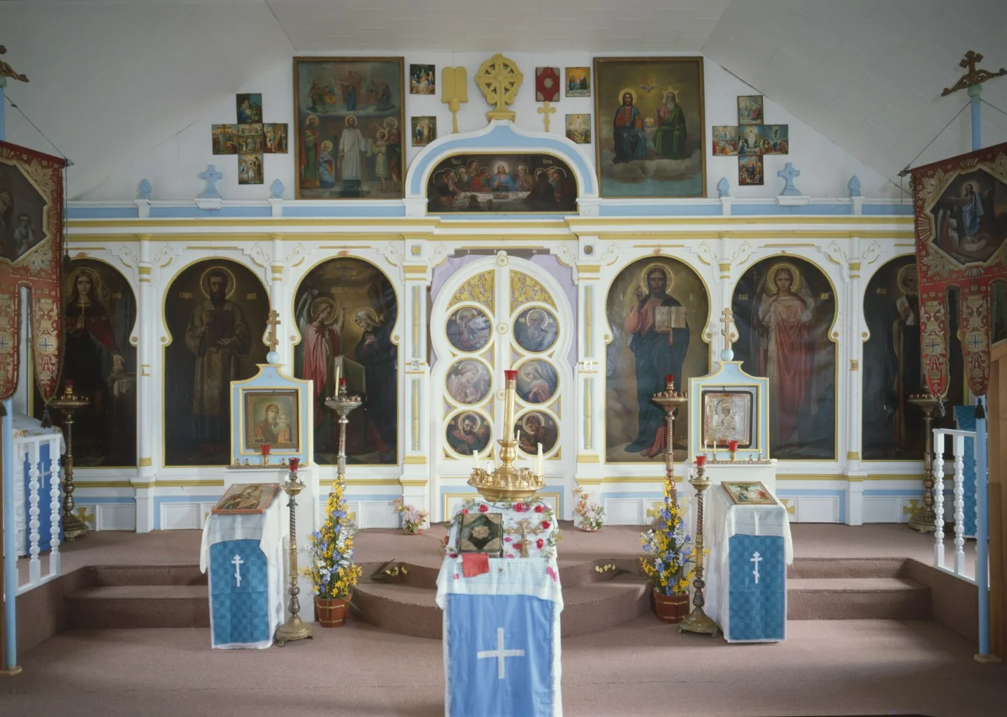 The nave of a small wooden church, looking east to a white and blue iconostasis with large icons of Christ, the Theotokos and the saints.