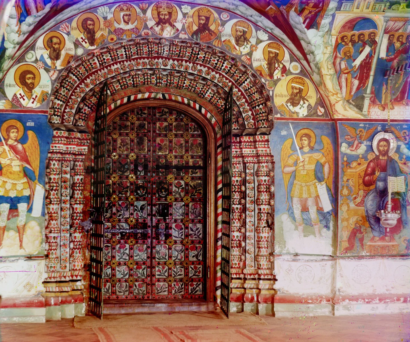 A carved and painted doorway into a church, with frescoes of saints and archangels on the walls around it.