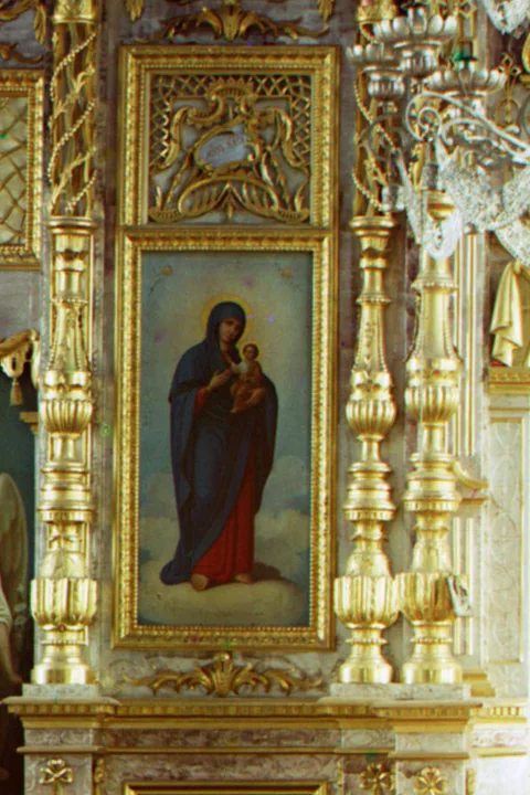 An icon of the Theotokos holding the Christ Child, in a gilded frame between carved golden columns on a church iconostasis.